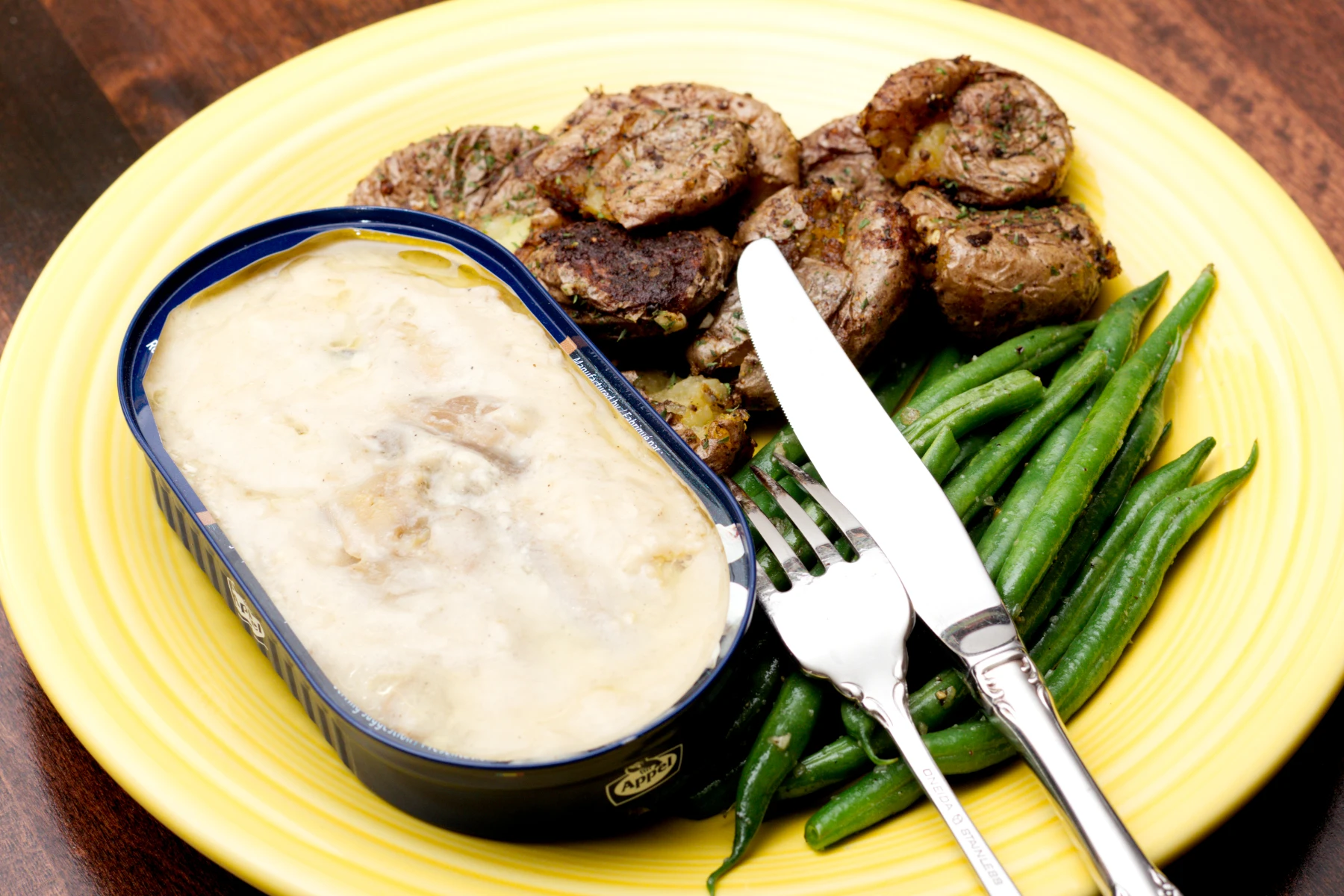 Opened tin on a plate with potatoes and green beans