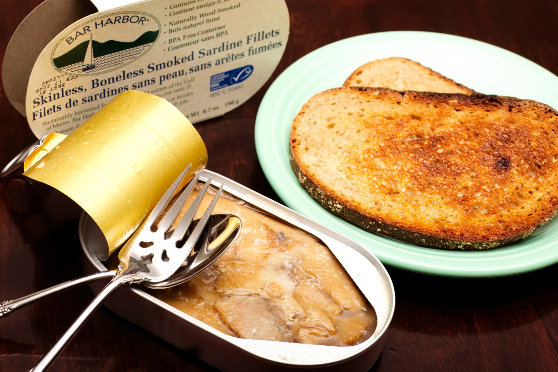 Opened tin of sardines with toasted rye bread on a plate.