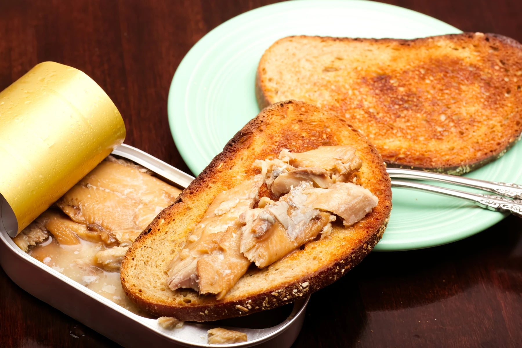 Sardine fillet morsels on toasted rye bread balanced on the tin.