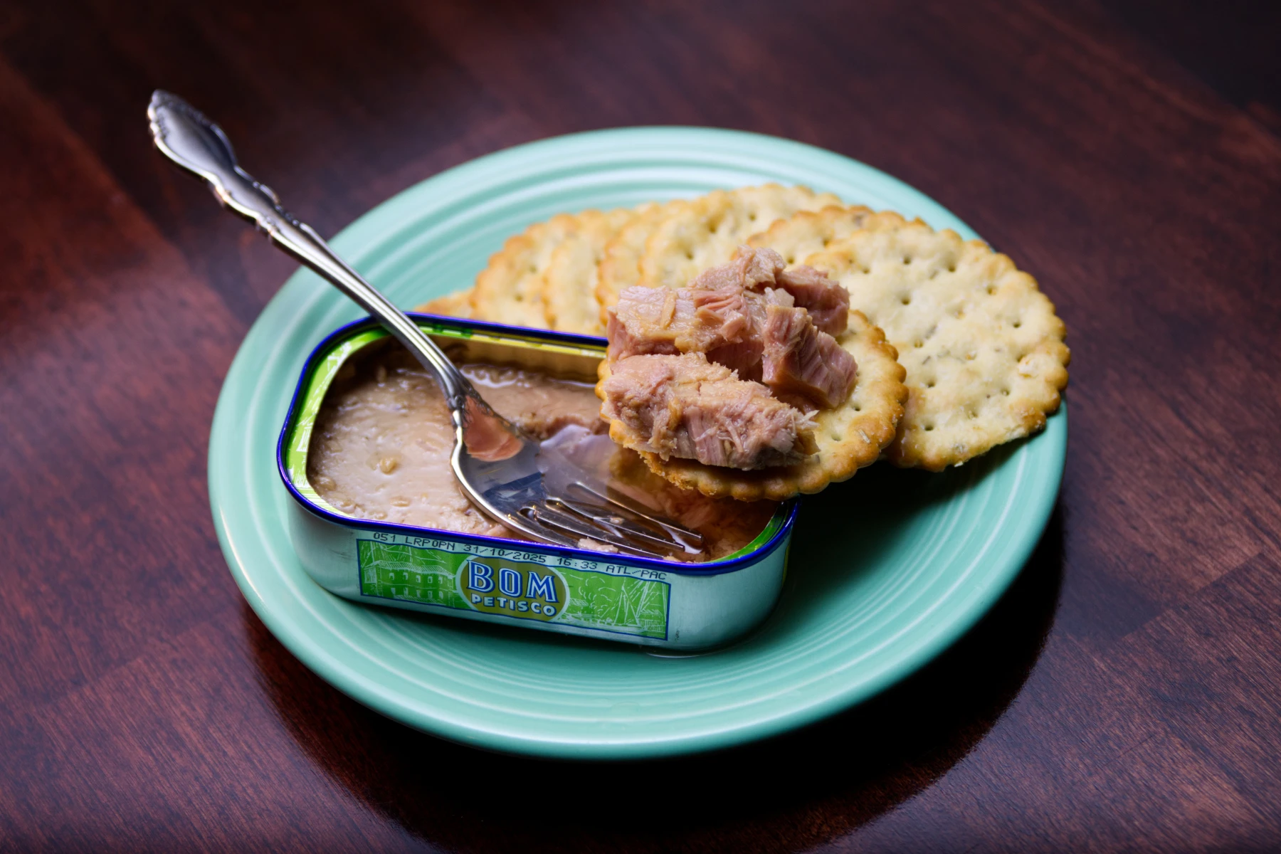 Some tuna chunks sitting on a cracker balanced on the rim of the fish tin