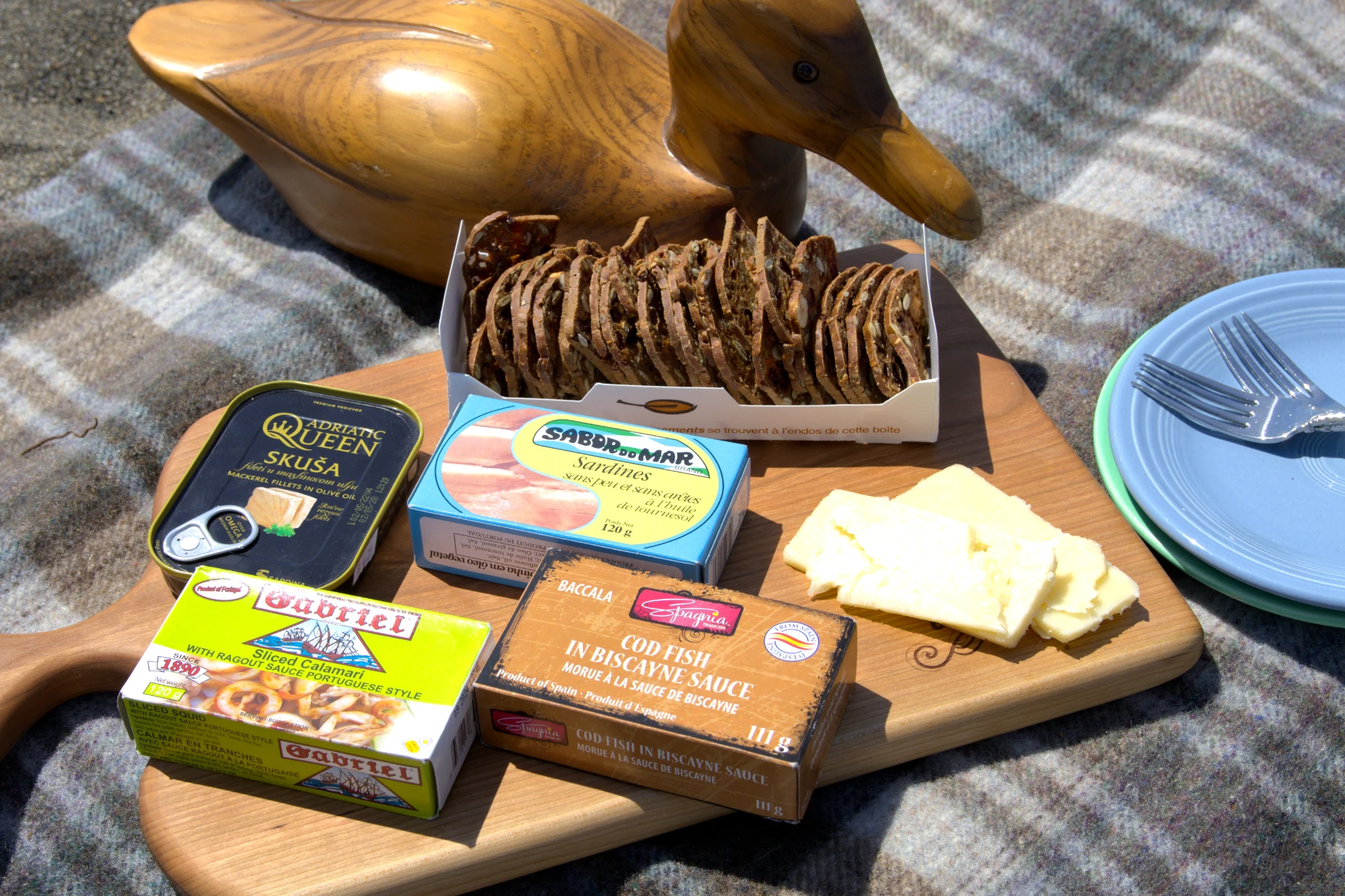 Four tins of fish on a charcuterie board with crackers and cheese