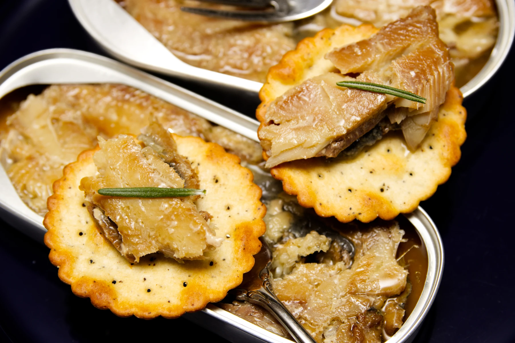 Pieces of kipper morsels ontop of crackers with rosemary sprigs.