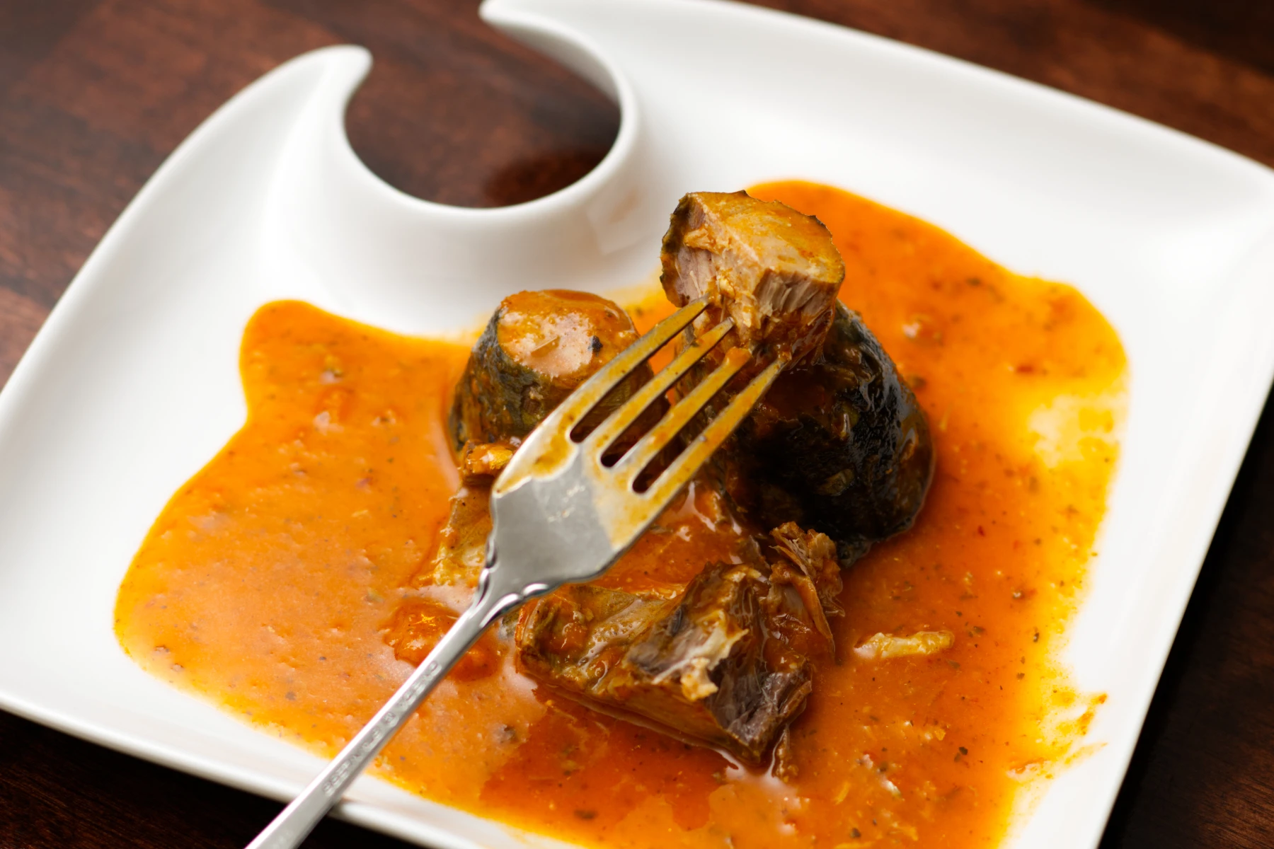 Piece of mackerel on a fork over a plate of sauce and more mackerel.