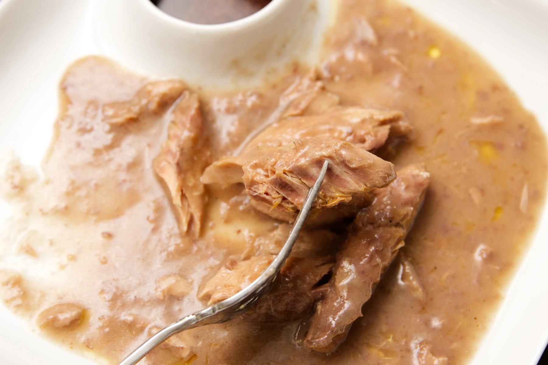 A morsel of mackerel on a fork covered in sauce.