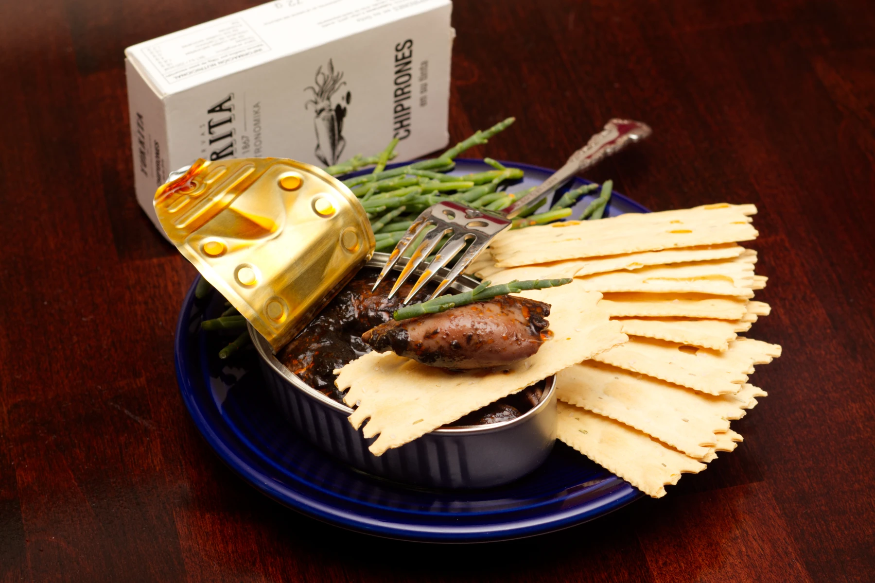 A piece of inky squid on a cracker with a piece of sea asparagus as garnish.
